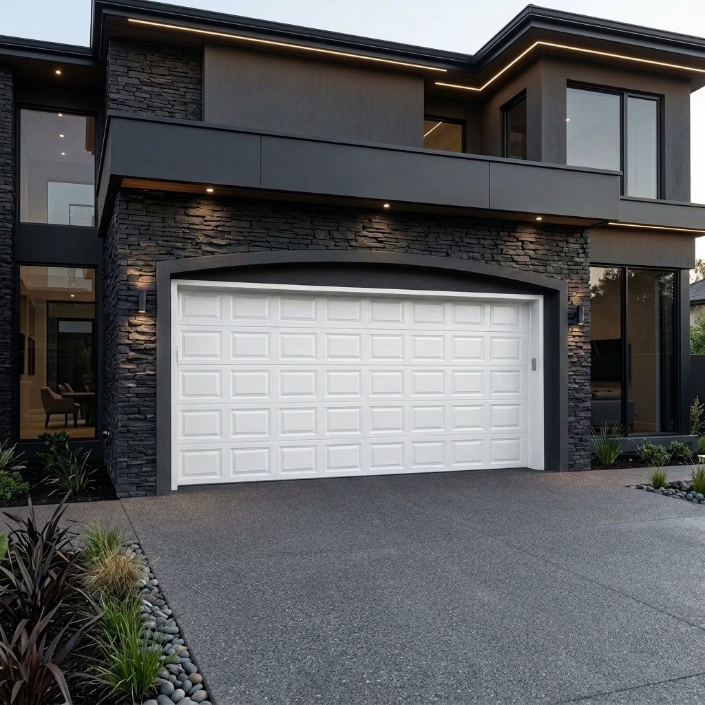 A modern white garage door installed on a contemporary dark gray house with stone veneer walls and a concrete driveway.