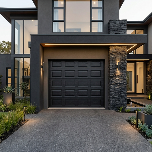 A modern black garage door set in a contemporary dark gray house with a stone pillar, large windows, and a concrete driveway.